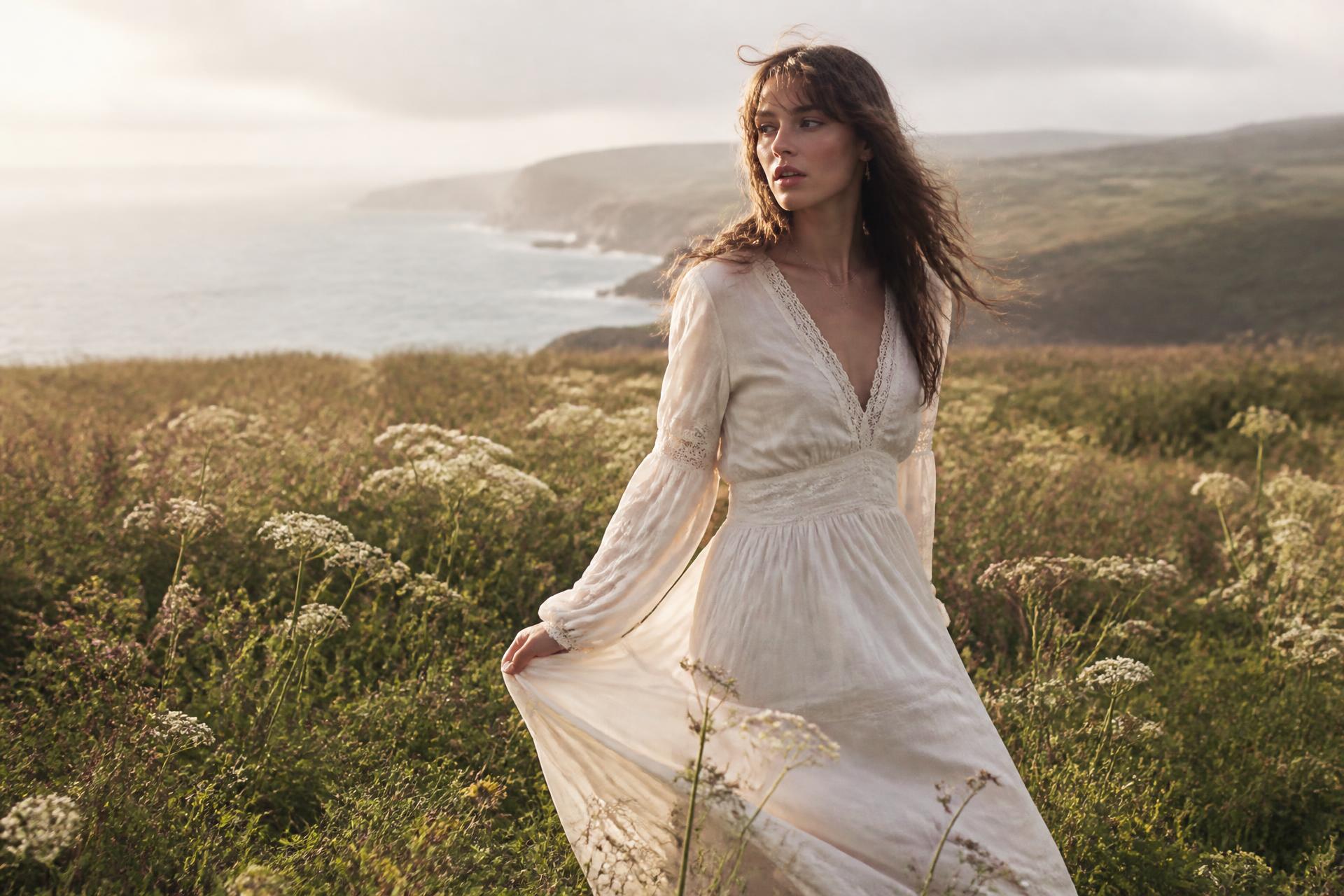 A woman in a cream dress walking through wildflowers on the Donegal coast